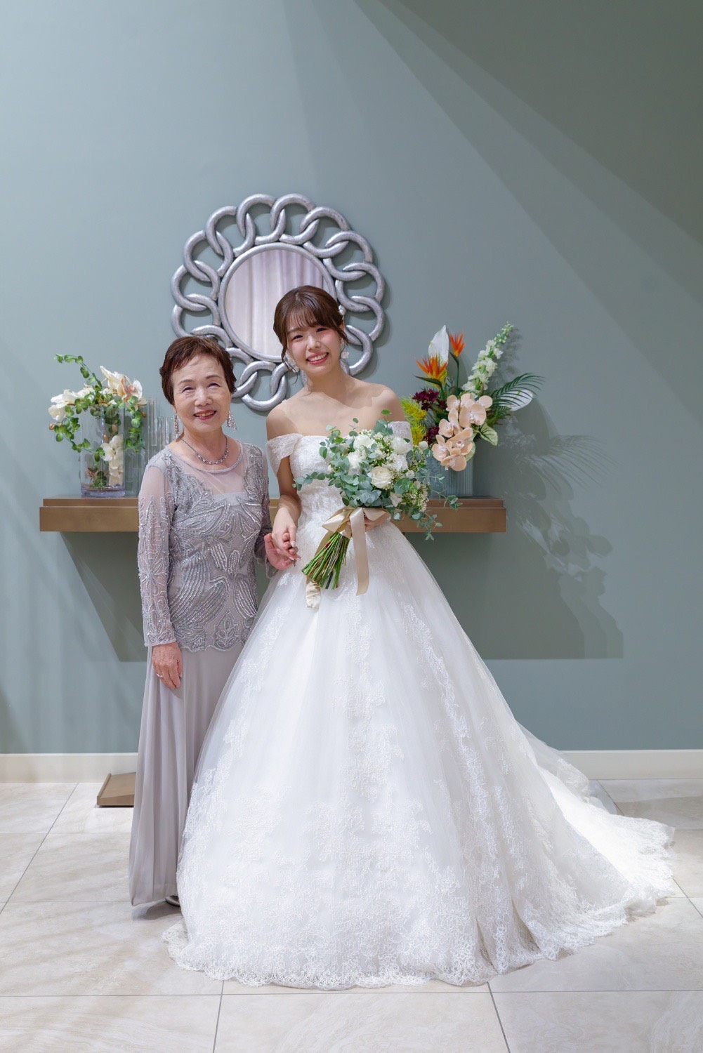 孫の結婚式でシルバーグレーのグランマドレスを着た祖母と純白のウエディングドレス姿の花嫁のツーショット