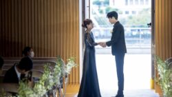 新郎母がネイビーのビジュードレスを着て、ジャケットセレモニーで新郎と手を取り合う感動的な瞬間。自然光に包まれた結婚式のワンシーン。