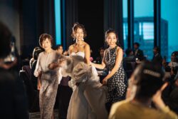 披露宴の中座で新婦が母と姉にエスコートされて歩くシーン。レースケープのマザードレスを着た新婦母とスタイリッシュなドレスの姉との美しいドレスアップ